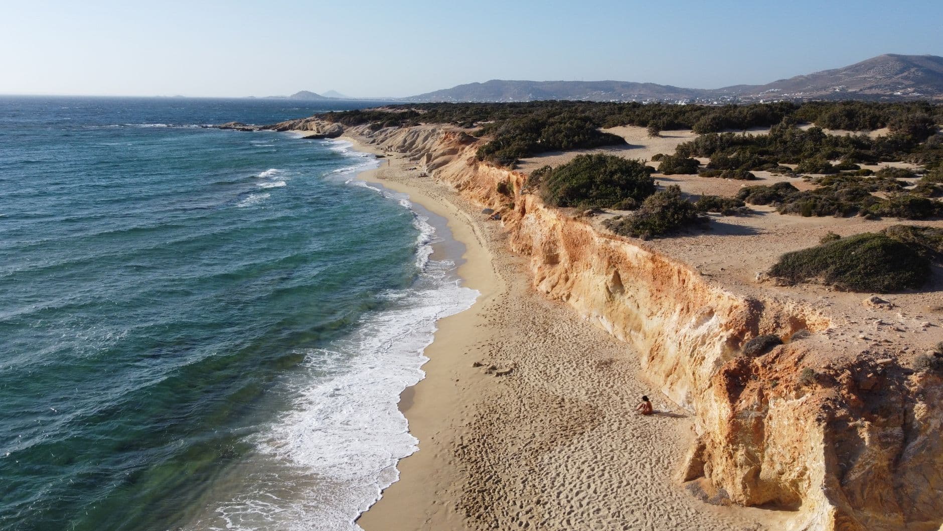 Zandstrand onder okerkleurige kliffen op Naxos