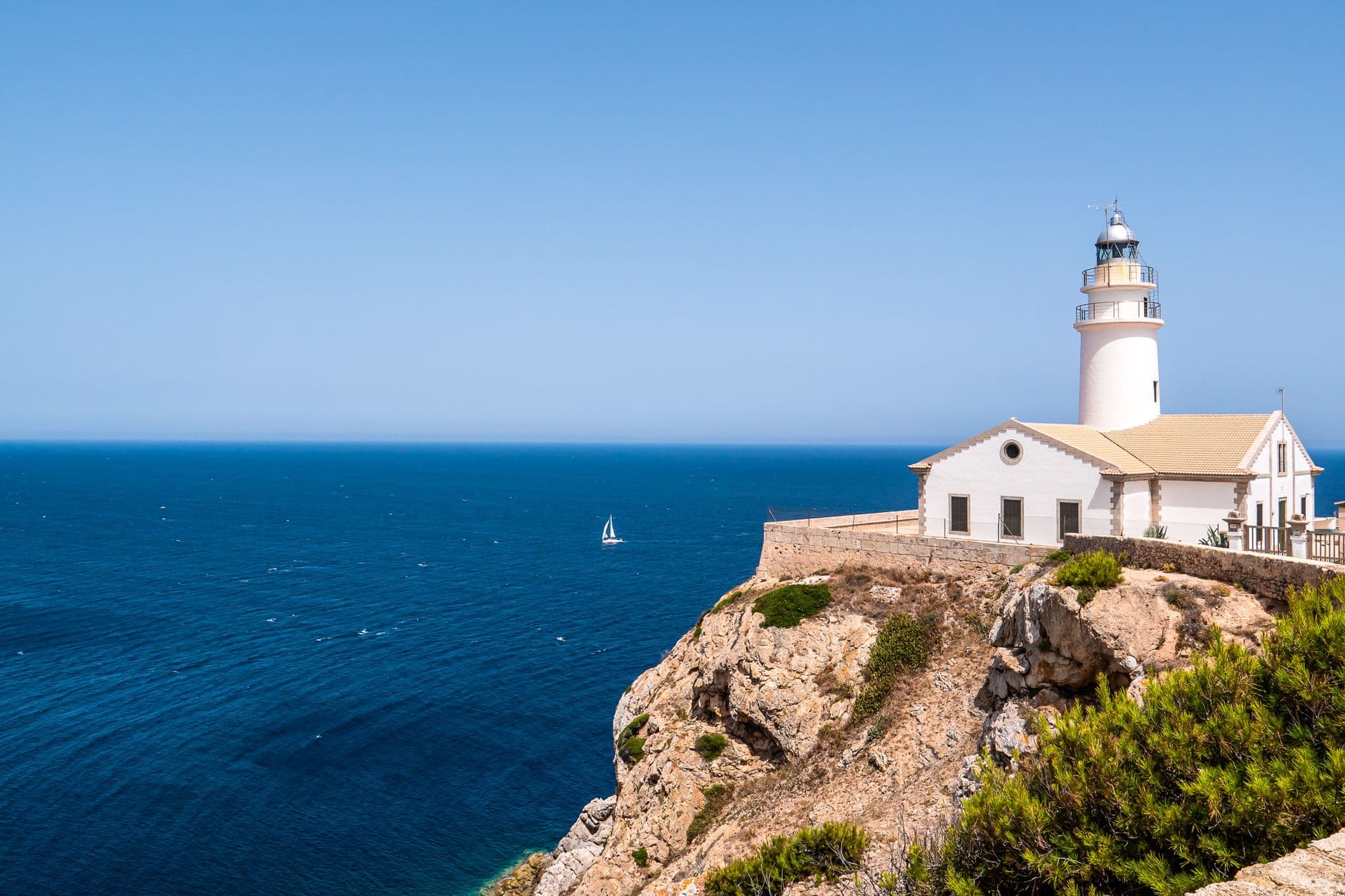 Een witte vuurtoren op een rotskaap aan de kust van Mallorca, met de blauwe zee erachter
