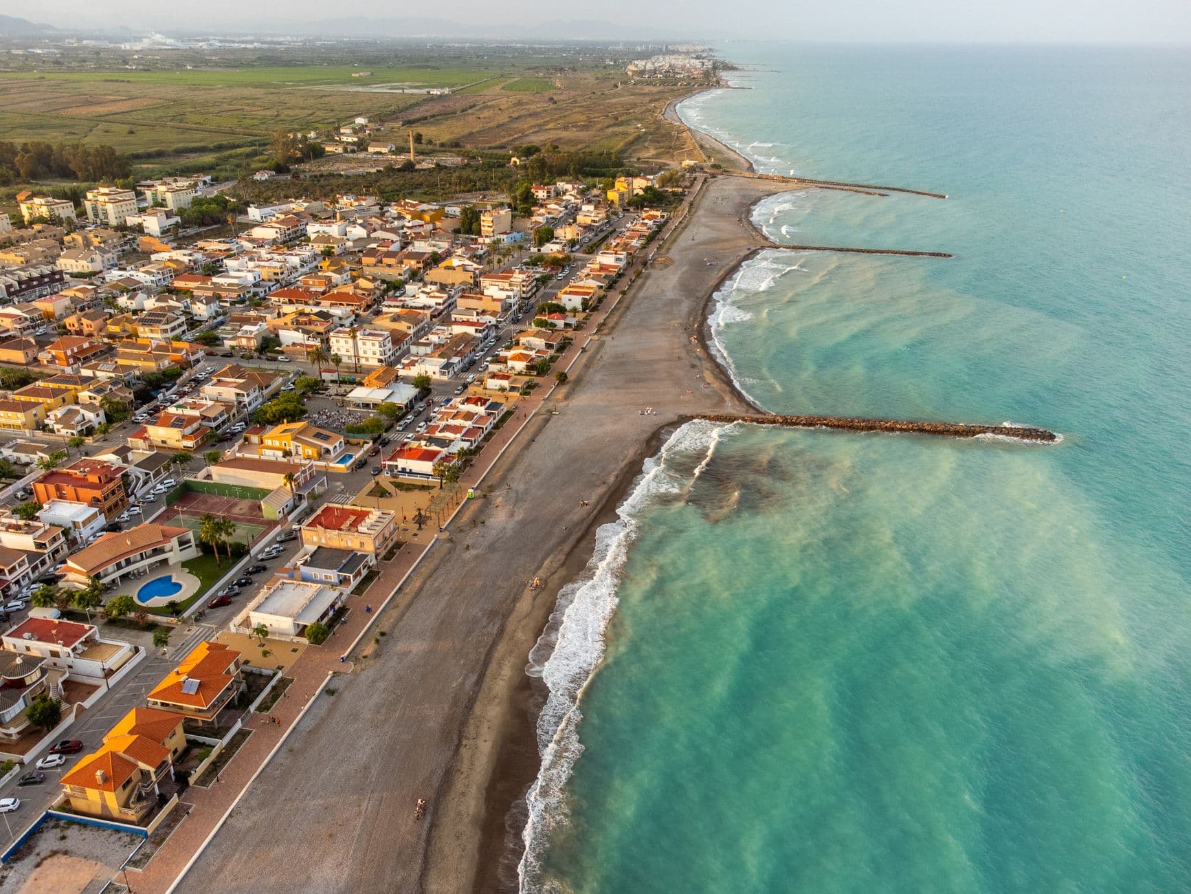 Luchtbeeld van een strand en kustplaats in de regio Valencia, met golfbrekers in zee