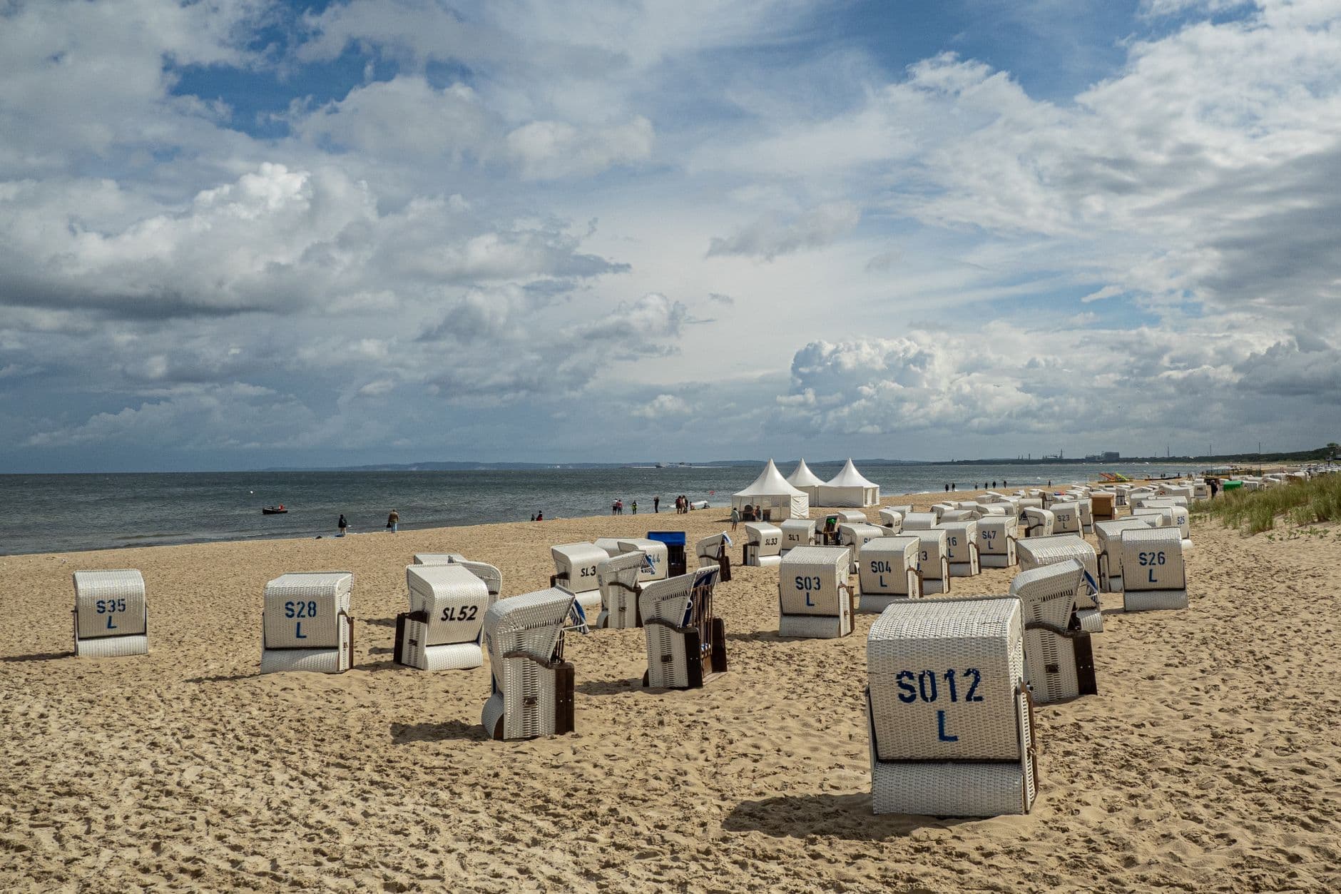 Serene beach scene with wicker chairs facing the sea under partly cloudy skies.