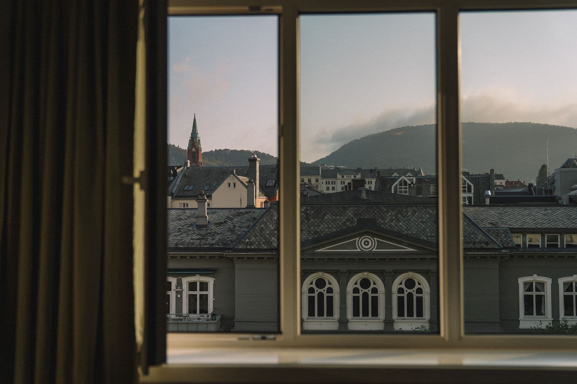 Charming view of Bergen's historic architecture from a window at dusk, featuring classic Scandinavian rooftops.