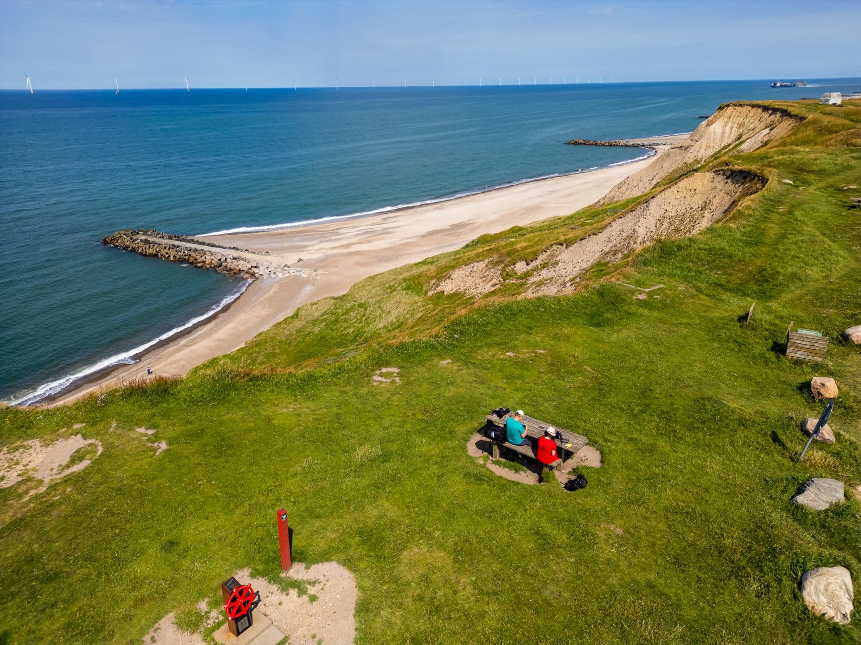 An aerial view of Denmark's coastline with a grassy cliff, beach, and two people at a picnic spot.