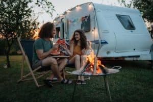 Koppel zit buiten aan een klein tafeltje voor hun caravan, genietend van een gezellige moment samen.