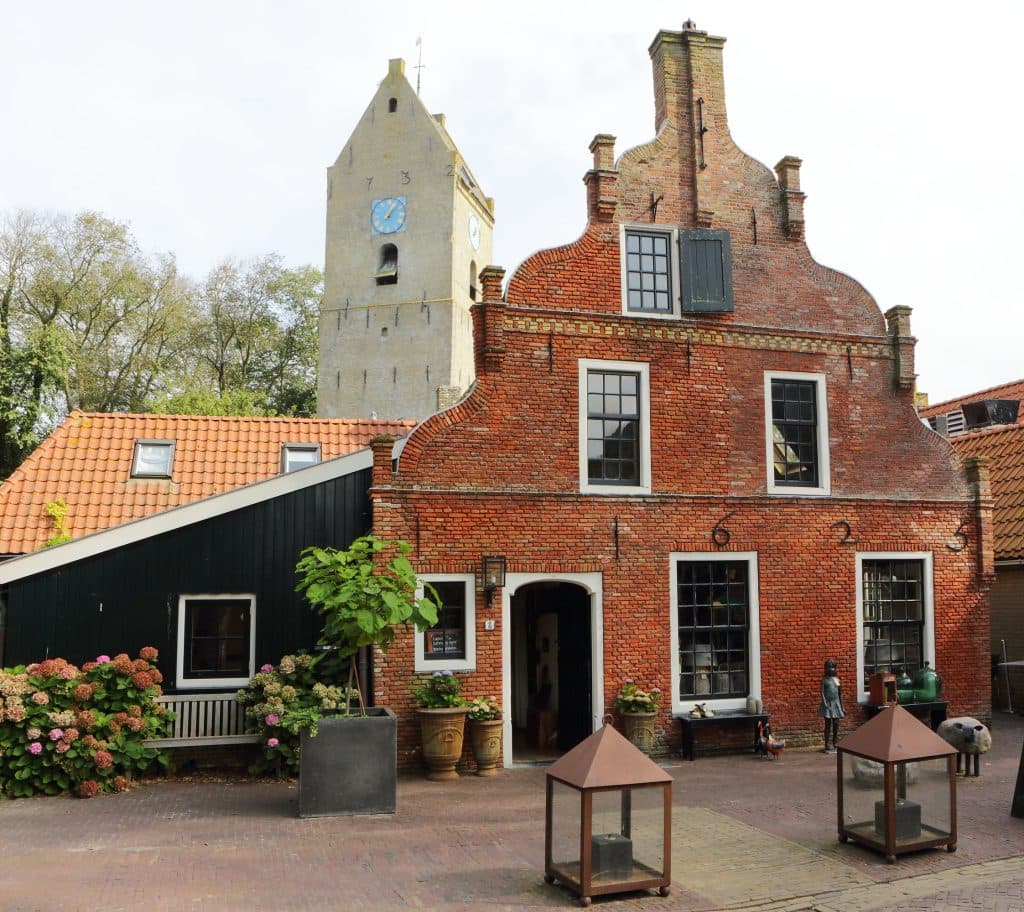 Een historische bakstenen gebouw met trapgevel en een toren met klok in een dorp