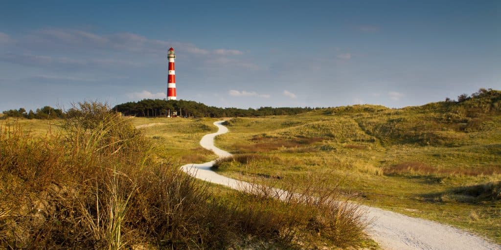 De rood-wit gestreepte Bornrif vuurtoren op Ameland, gezien vanaf een wit stenen pad door duingras