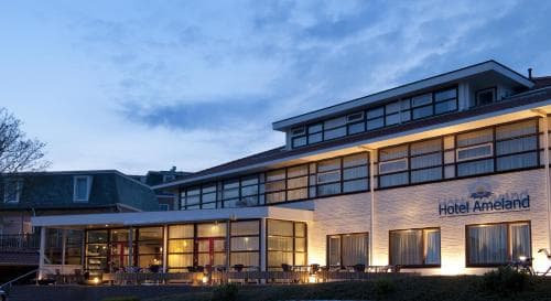 Hotel Ameland gebouw bij schemering met verlichte ramen en terras.