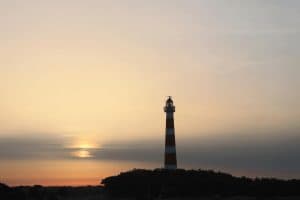 De rood-wit gestreepte vuurtoren Bornrif op Ameland bij zonsondergang, met de zon achter de wolken
