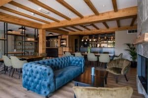 Een ruim interieur met houten balkenplafond, een blauwe Chesterfield-bank, en beige stoelen aan tafels