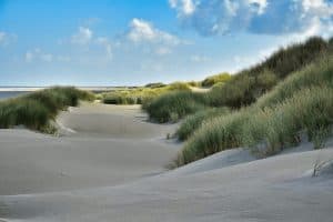 Duinlandschap met wit zand, groen helmgras en blauwe lucht met wolken
