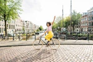 Vrouw fietst over een traditionele Nederlandse brug met een schilderachtige omgeving van grachten en huizen.